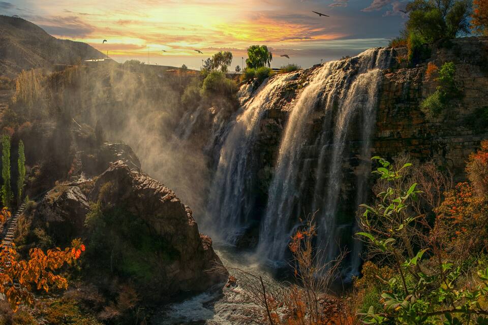 A waterfall cascading down a rocky cliff surrounded by autumn foliage.