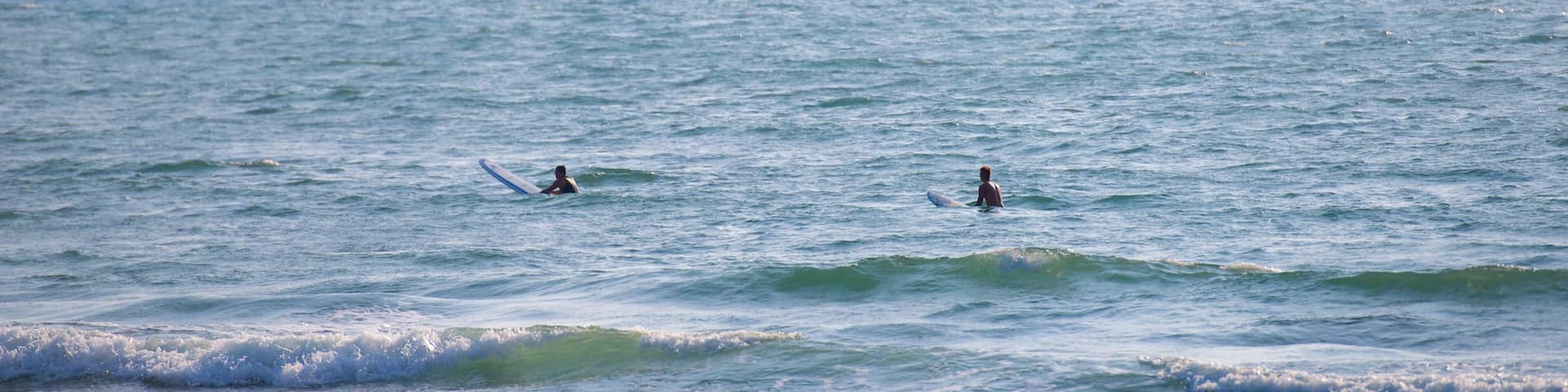Two surfers in the ocean with ships in the background.