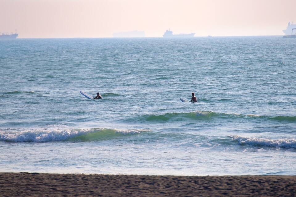 Twee surfers in de oceaan, met schepen op de achtergrond.