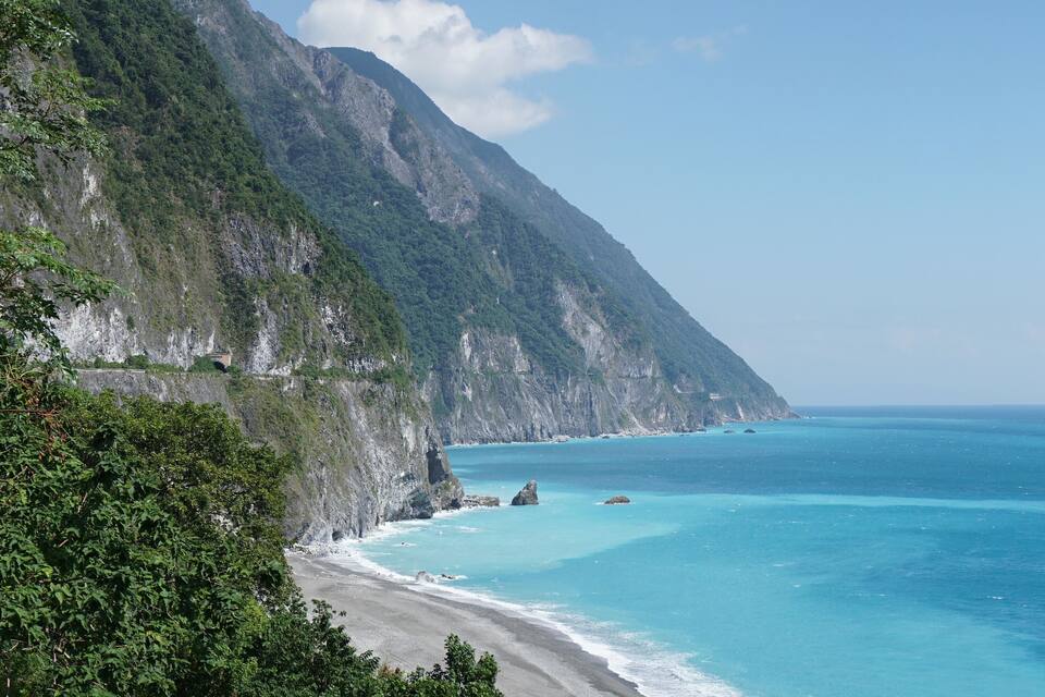 Paesaggio costiero con una scogliera ripida, mare color turchese e vegetazione lussureggiante.