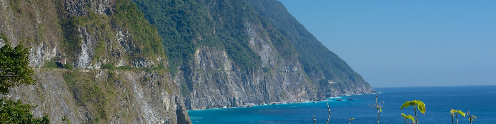 A coastal landscape with steep cliffs, a clear blue sea, and lush greenery.