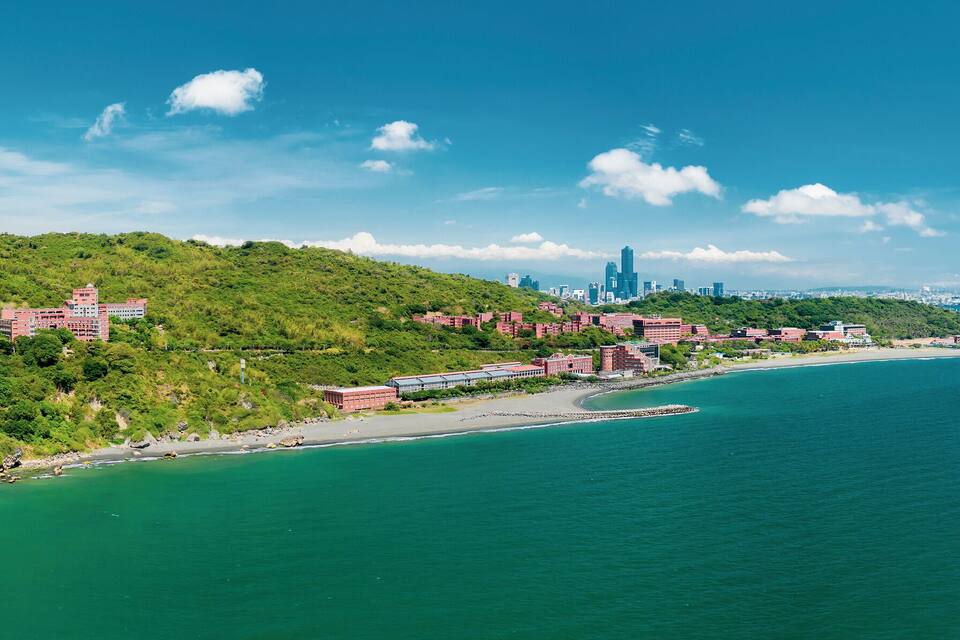 A coastal city with a prominent skyscraper, a beach, and lush green hills.