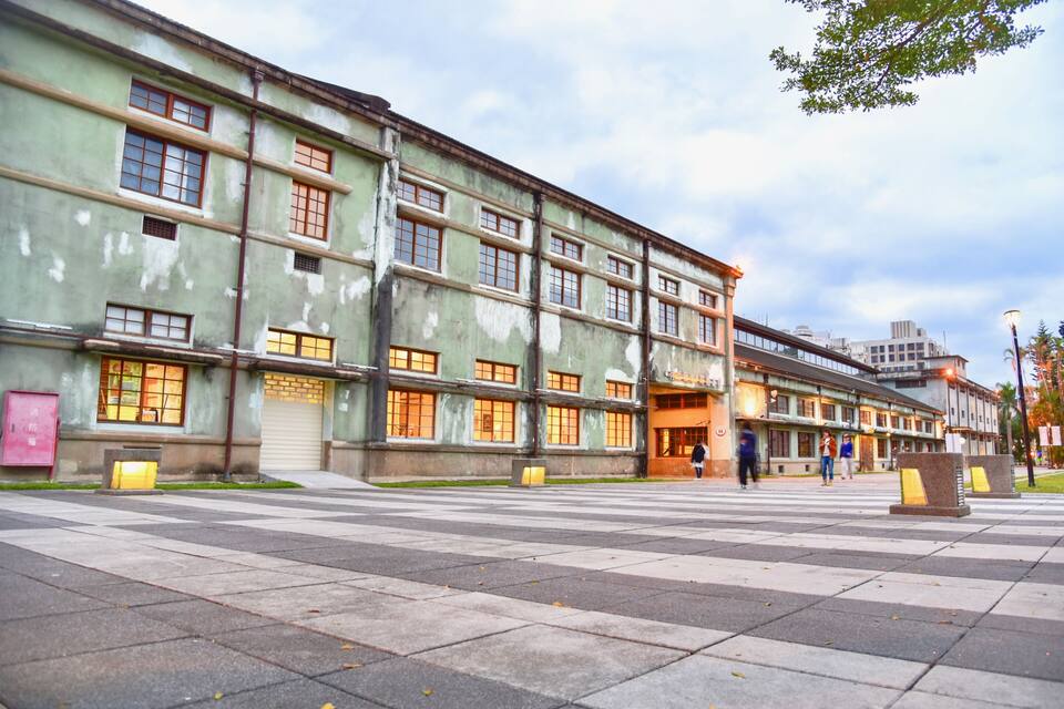 A large, historic building with multiple windows and a paved plaza in front.