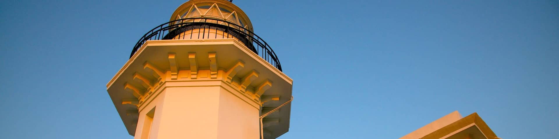 A lighthouse with a white tower and a balcony, set against a clear blue sky.