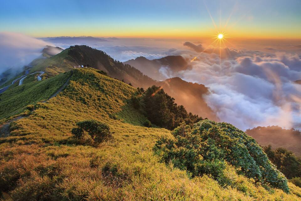 A sunrise over a mountainous landscape with a road winding through the hills.