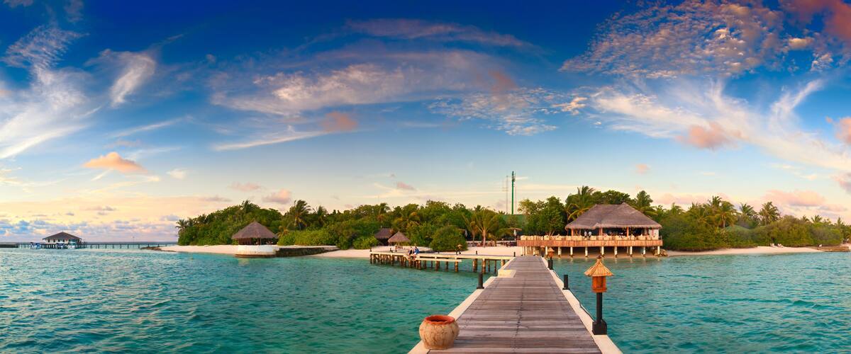A wooden pier leading to overwater bungalows surrounded by turquoise waters and palm trees.