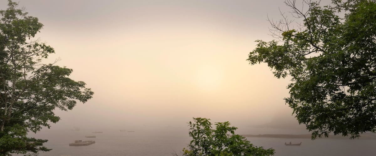 Foggy morning seascape with empty bench and table on the green hill at Boothbay Harbor in Lincoln County, Maine