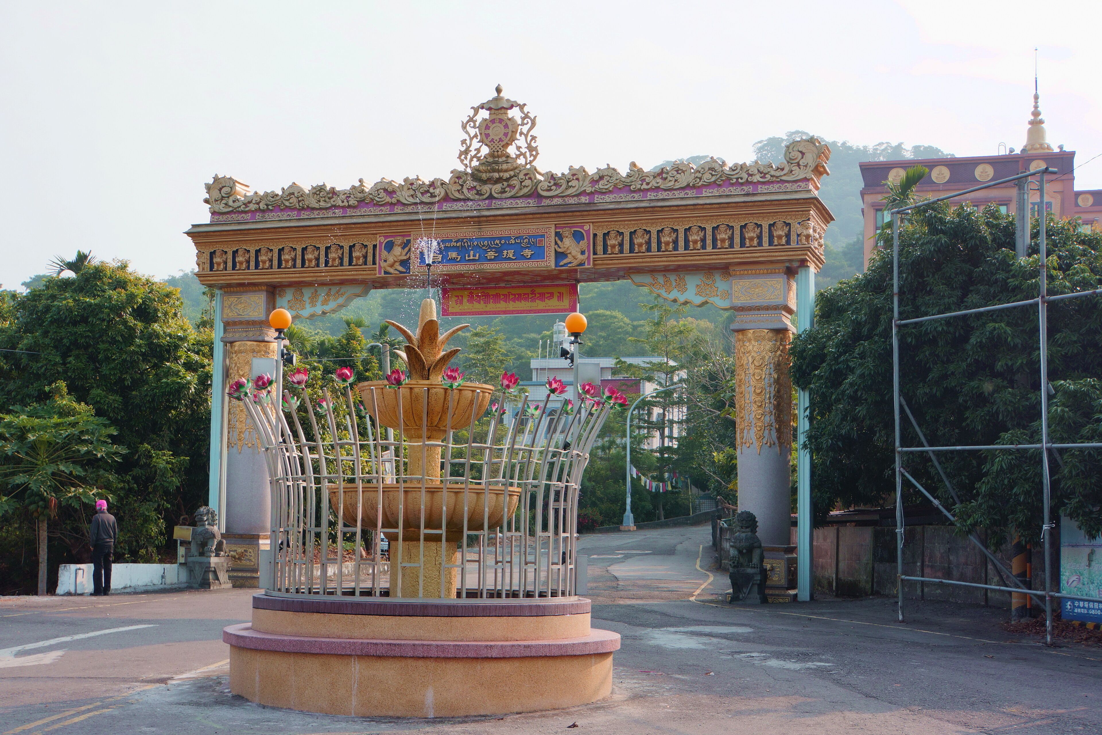 A traditional gate with ornate decorations and a central fountain with flowers.