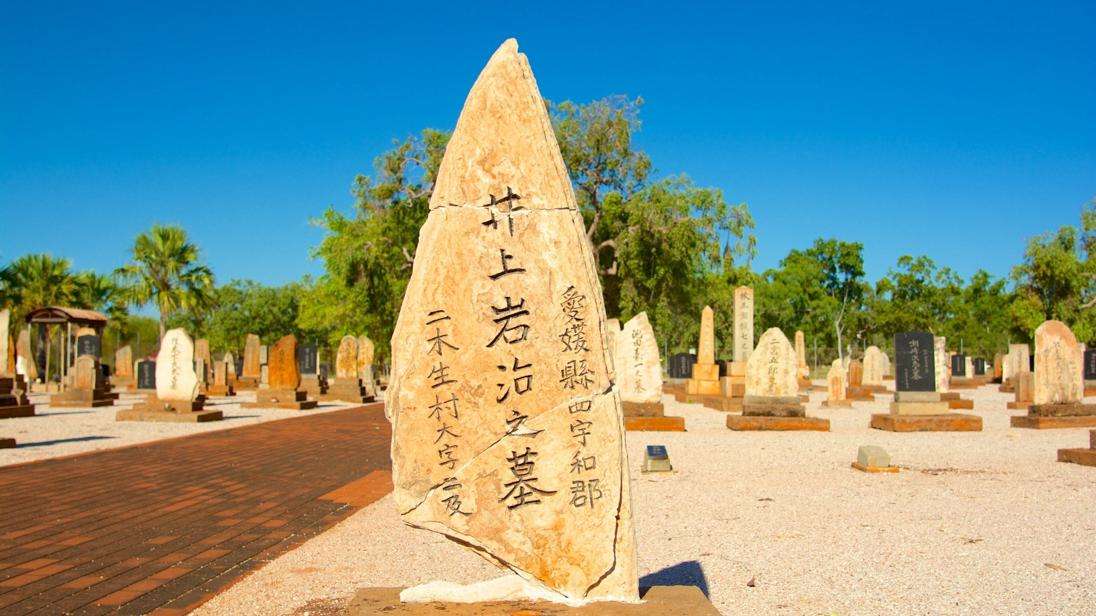 A stone monument with inscriptions in a cemetery surrounded by trees and other gravestones.