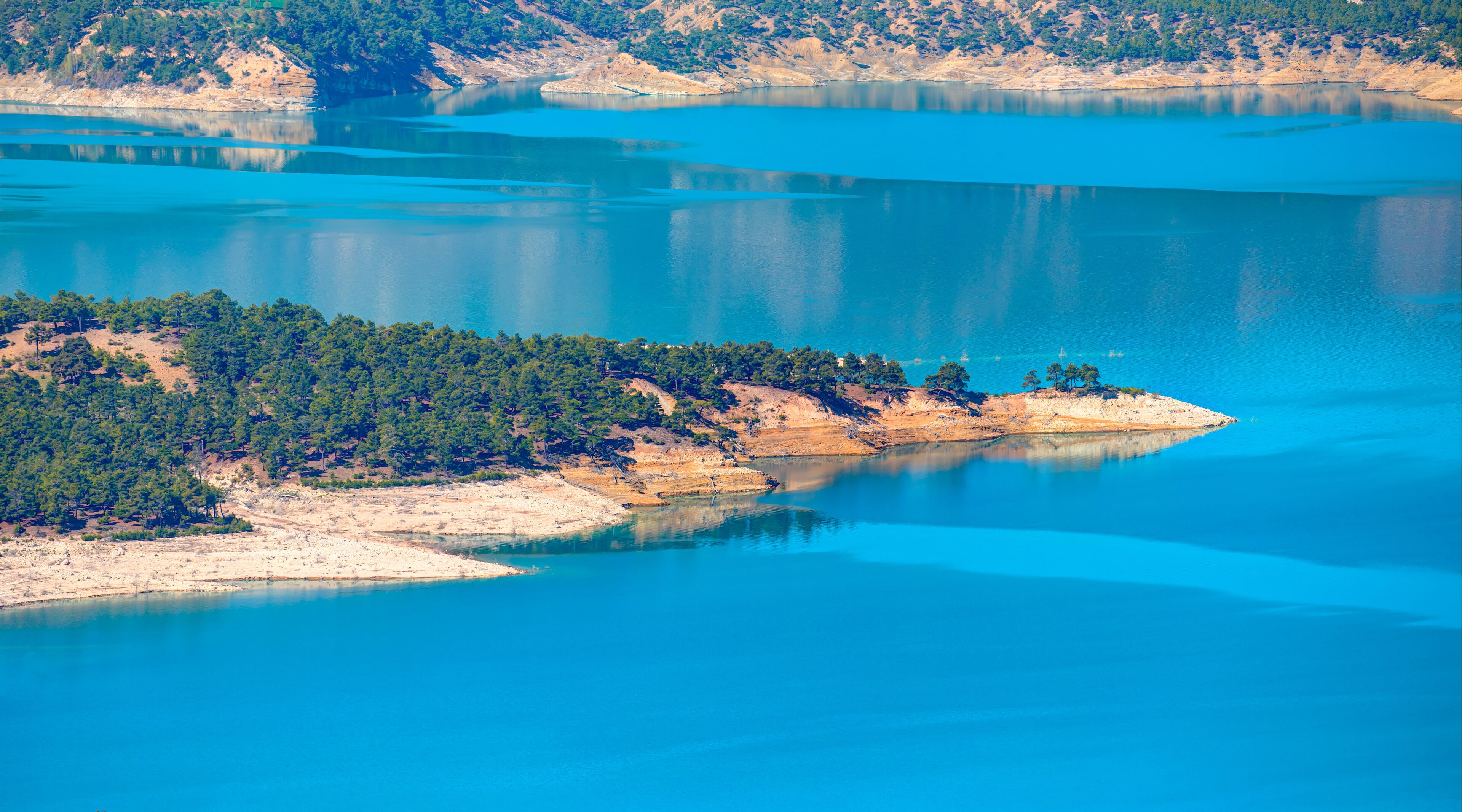 A turquoise lake with a forested island and surrounding hills.