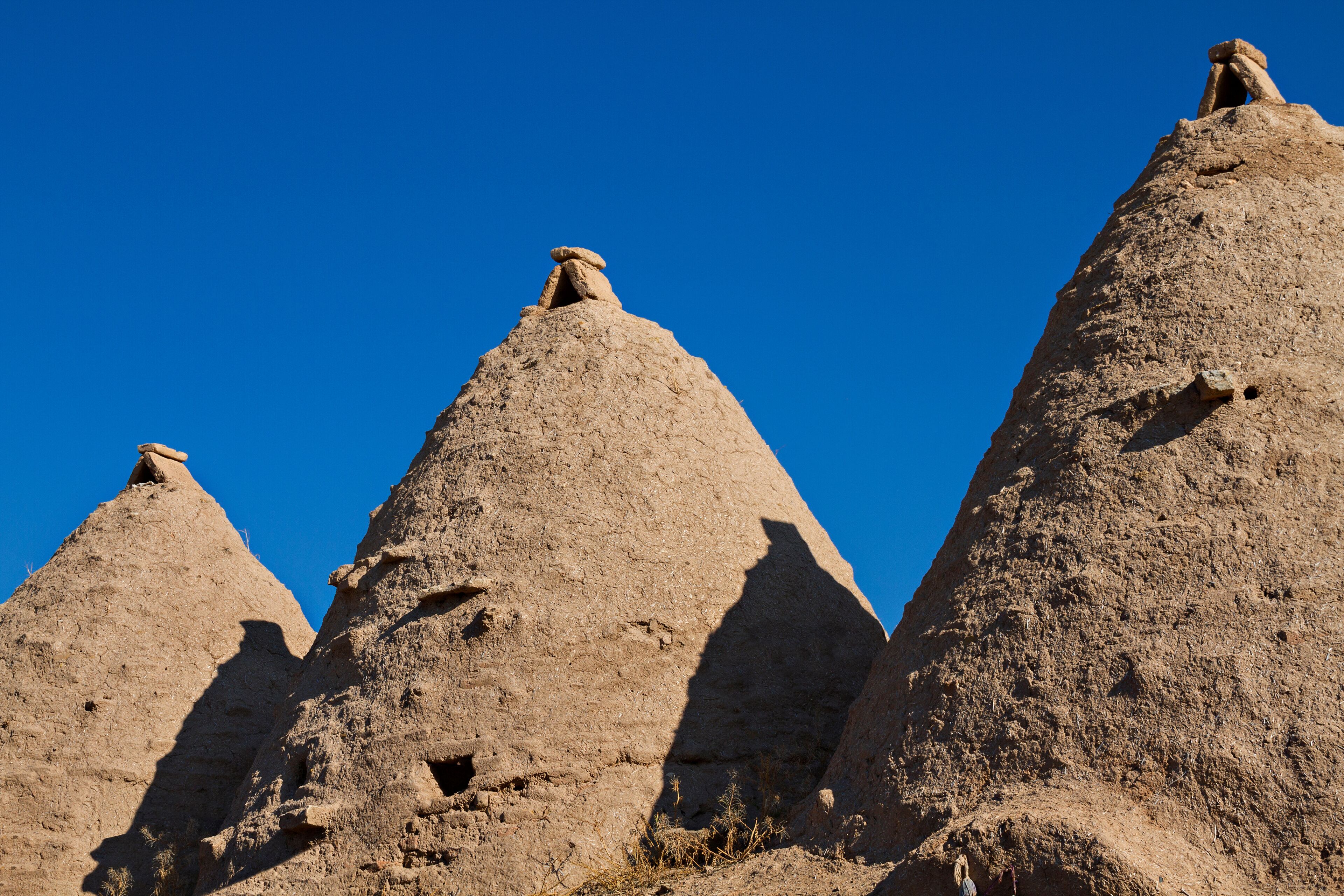 Three large, conical rock formations with shadows cast on them, set against a clear blue sky.