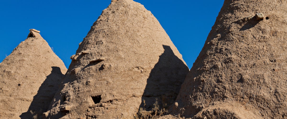 Three large, conical rock formations with shadows cast on them, set against a clear blue sky.