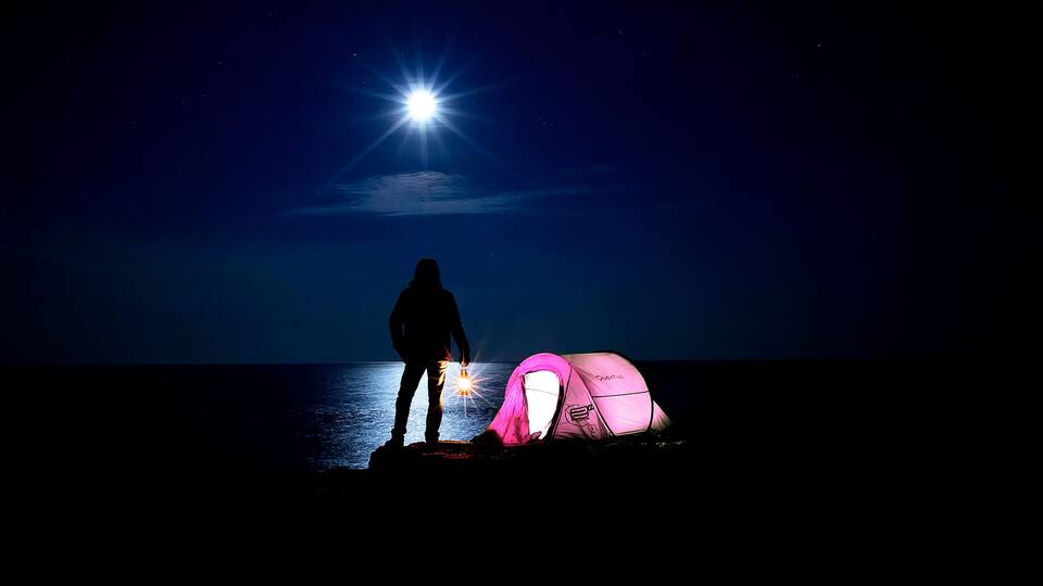 A person standing by a tent under a bright moonlit sky.