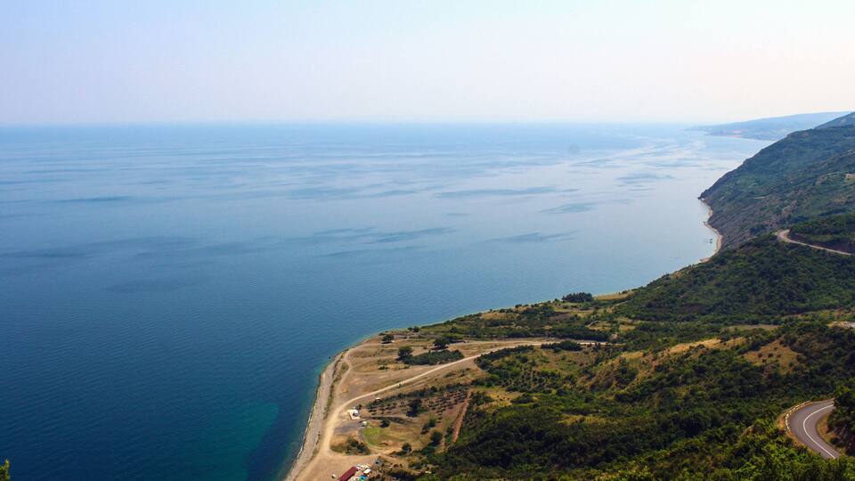 A coastal landscape with a winding road, a beach, and a view of the sea.