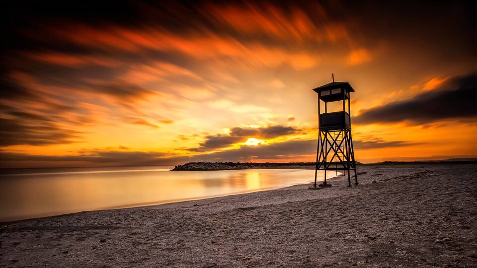 A beach with a lighthouse at sunset.