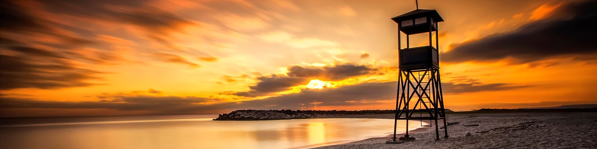 Una playa con un faro al atardecer.