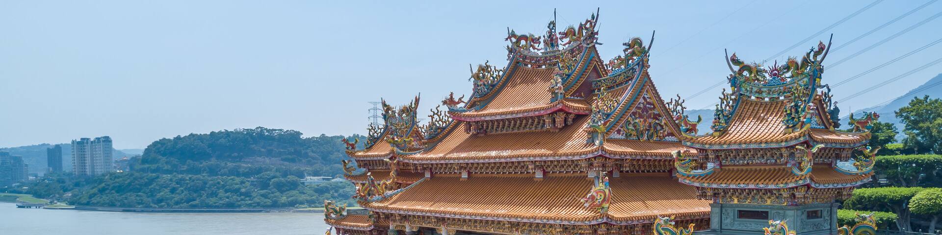 A traditional multi-tiered temple with ornate roofs and intricate carvings, situated by a body of water.
