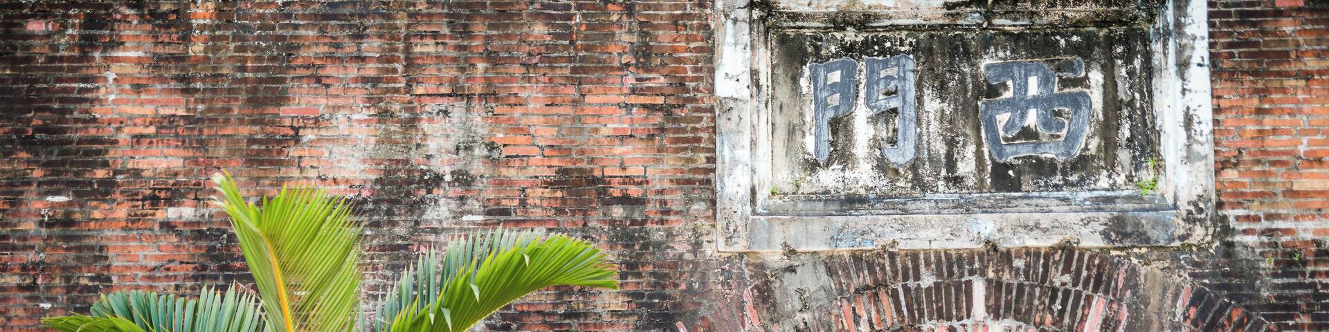 Un arco de ladrillo con una palmera en primer plano y un letrero con caracteres chinos.