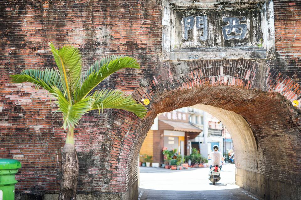 A brick archway with a palm tree in the foreground and a sign with Chinese characters.