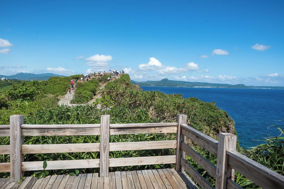 A wooden boardwalk with a view of the ocean and a distant mountain range.
