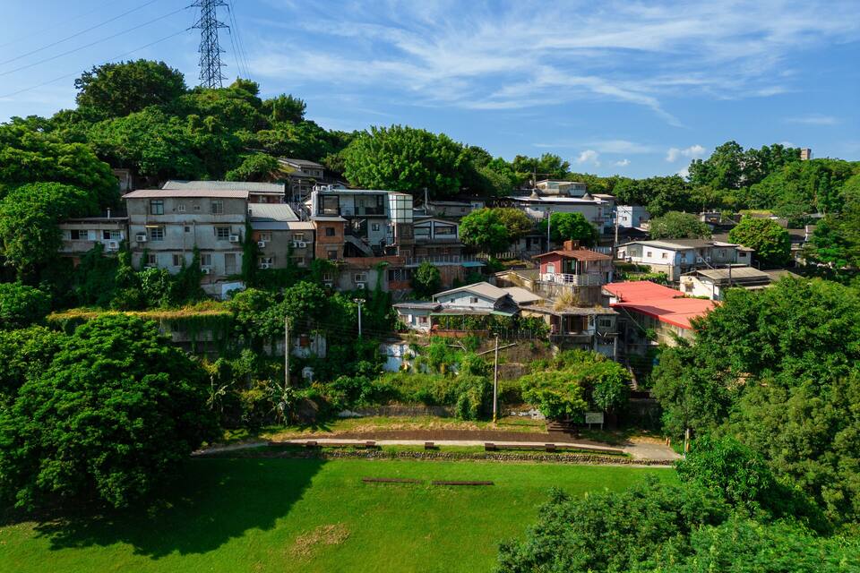 Un pueblo en una ladera con abundante vegetación, casas y una torre de líneas eléctricas.
