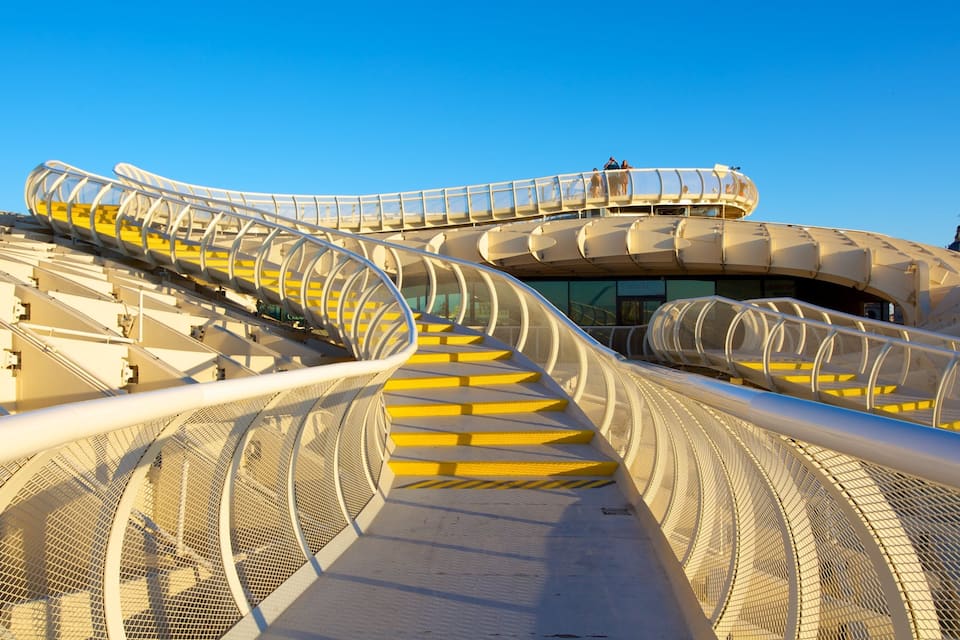 A spiraling pedestrian bridge with yellow steps and a mesh railing.