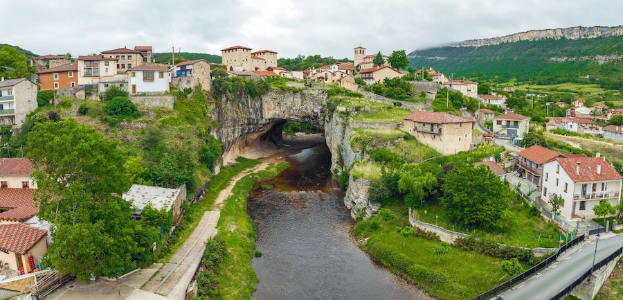 A town with a river, stone bridge, and buildings on a hillside.