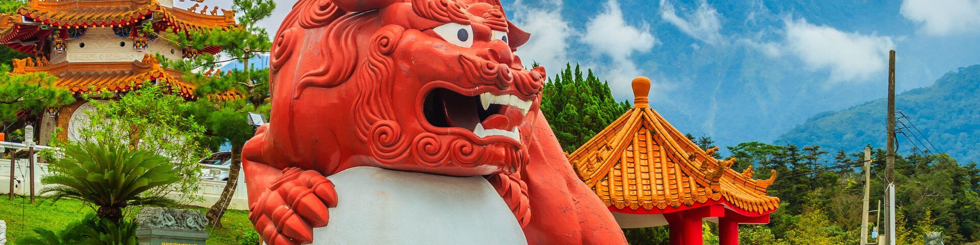 A large red lion statue, a traditional Chinese temple, and a mountain in the background.
