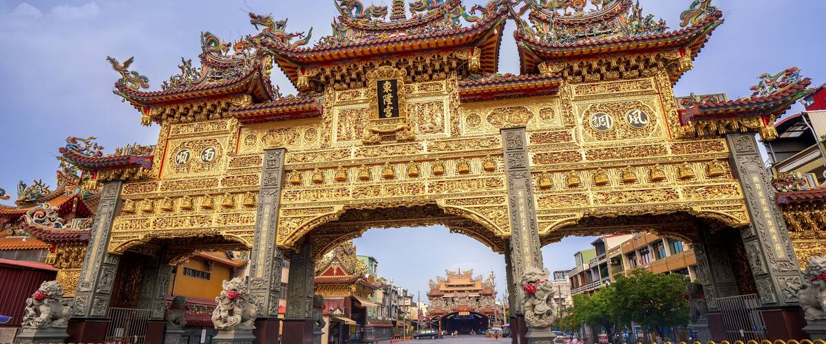 A golden ornate gate with dragons, traditional architecture, and a clear sky.