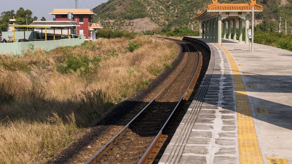A railway track curving to the right, with a platform on the right side and a building with a yellow roof in the background.