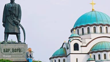 Estátua de um homem com um livro, identificada como "Kapahopke", e uma igreja com cúpulas azuis.