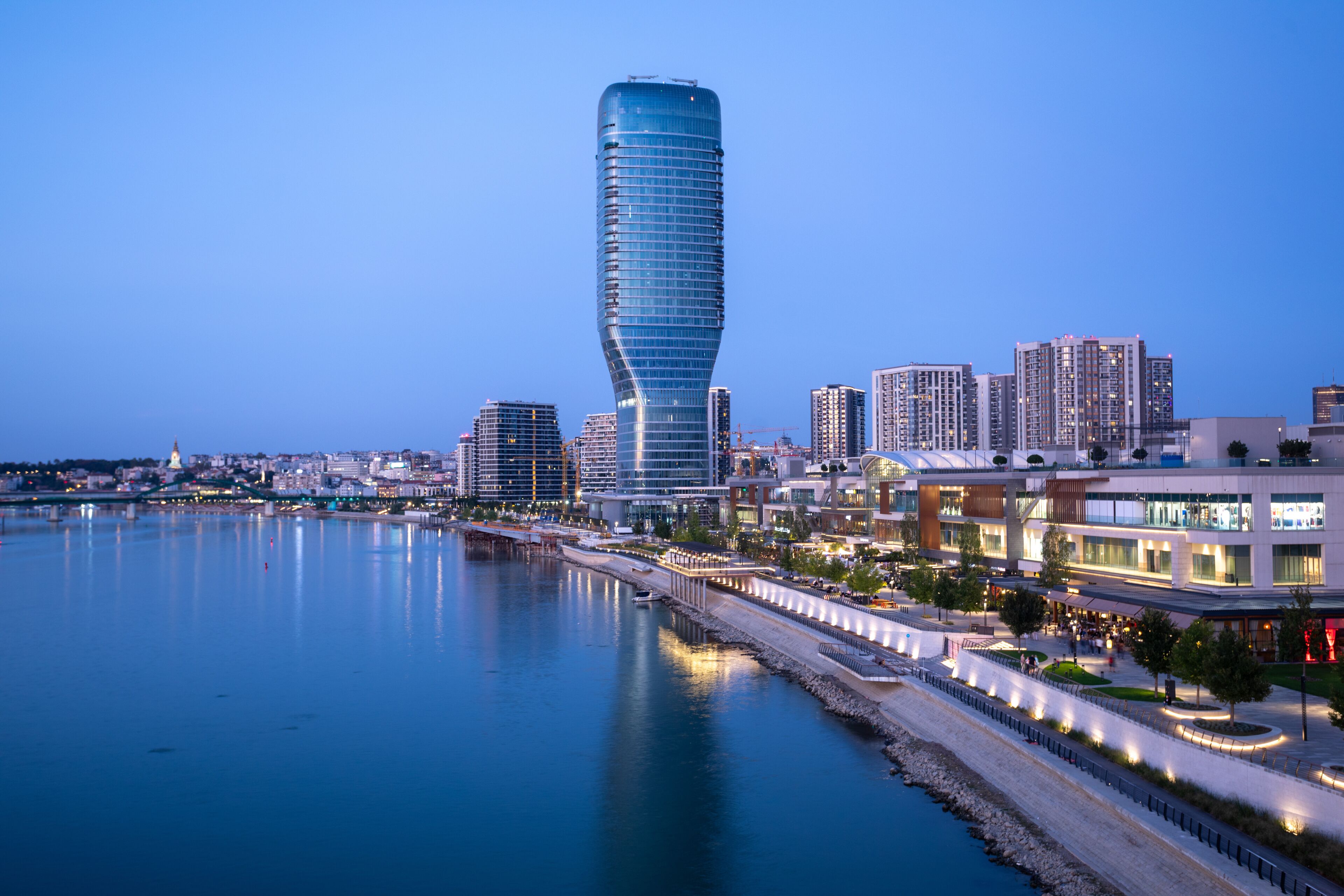 Un horizonte urbano con un rascacielos distintivo y retorcido, un paseo marítimo y edificios modernos a lo largo del río.