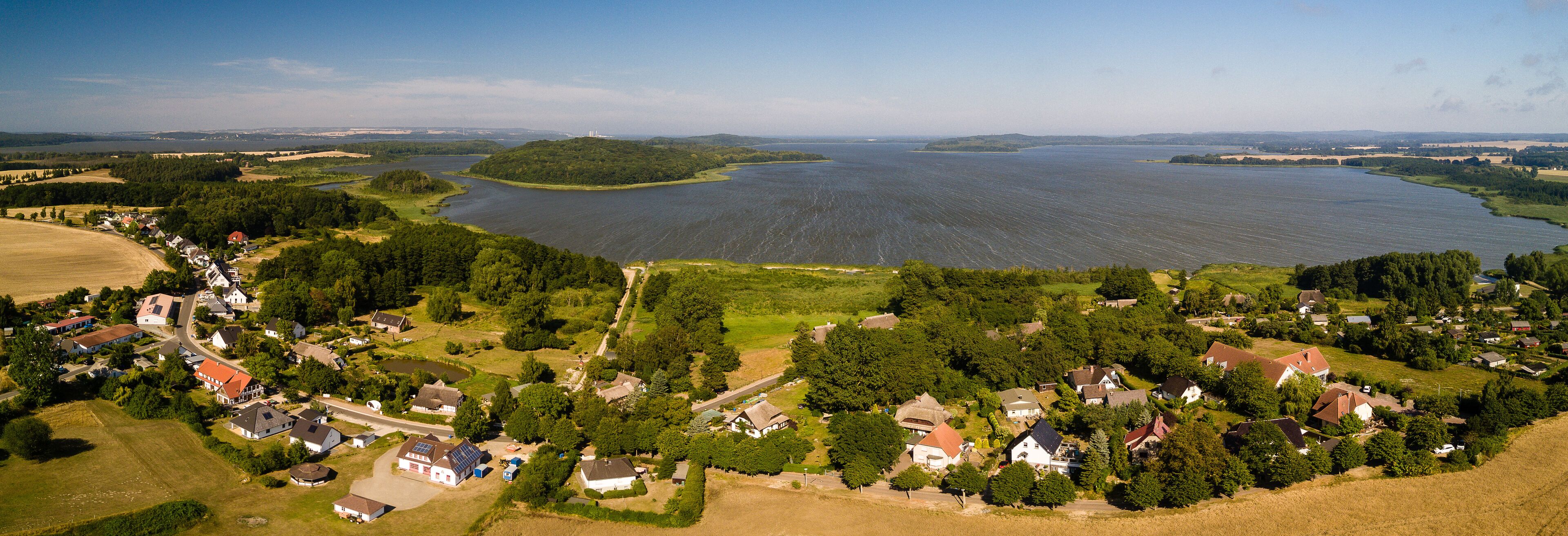 A lakeside village with houses, a river, and surrounding greenery.