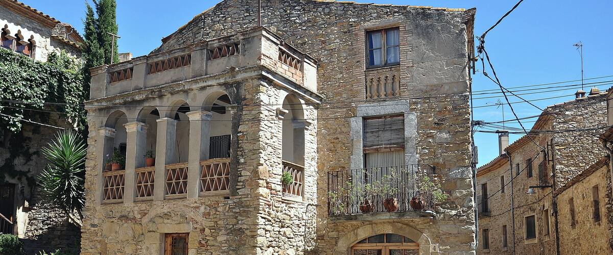 A stone building with arched windows and balconies, surrounded by narrow streets and other historic buildings.