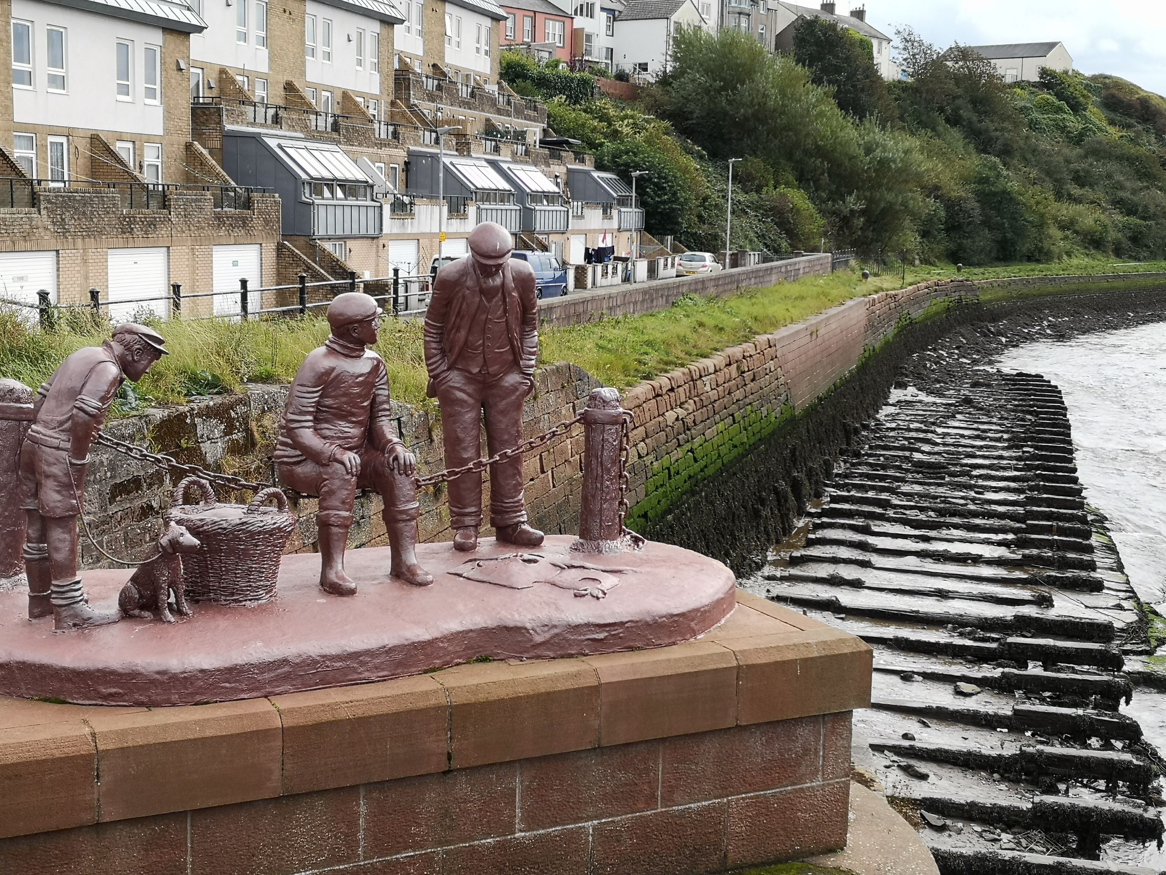 A bronze statue of workers by a coastal walkway.