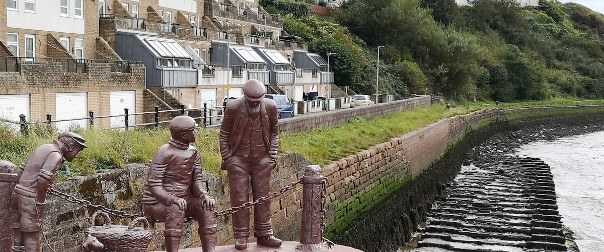 A bronze statue of workers by a coastal walkway.