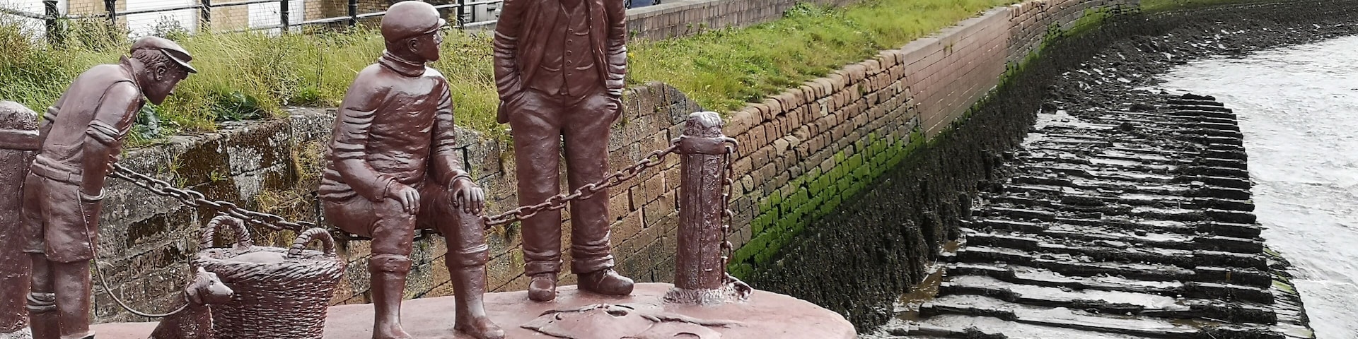 A bronze statue of workers by a coastal walkway.