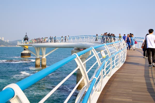 A pier with a blue railing, people walking, and a lighthouse in the background.