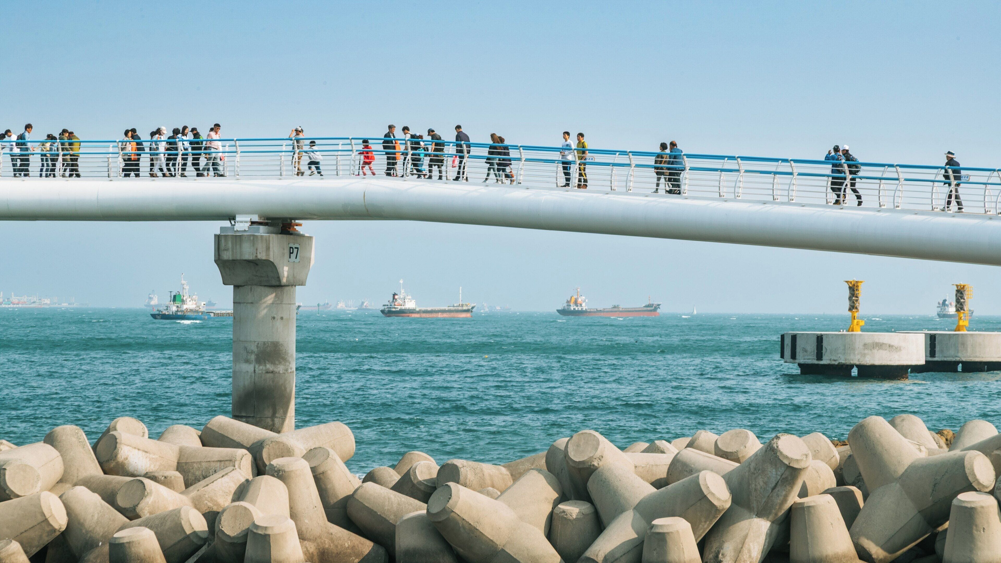 Visitors stroll along the iconic bridge at Songdo Beach in Seo, Busan, South Korea, enjoying the vibrant coastal atmosphere and stunning ocean views