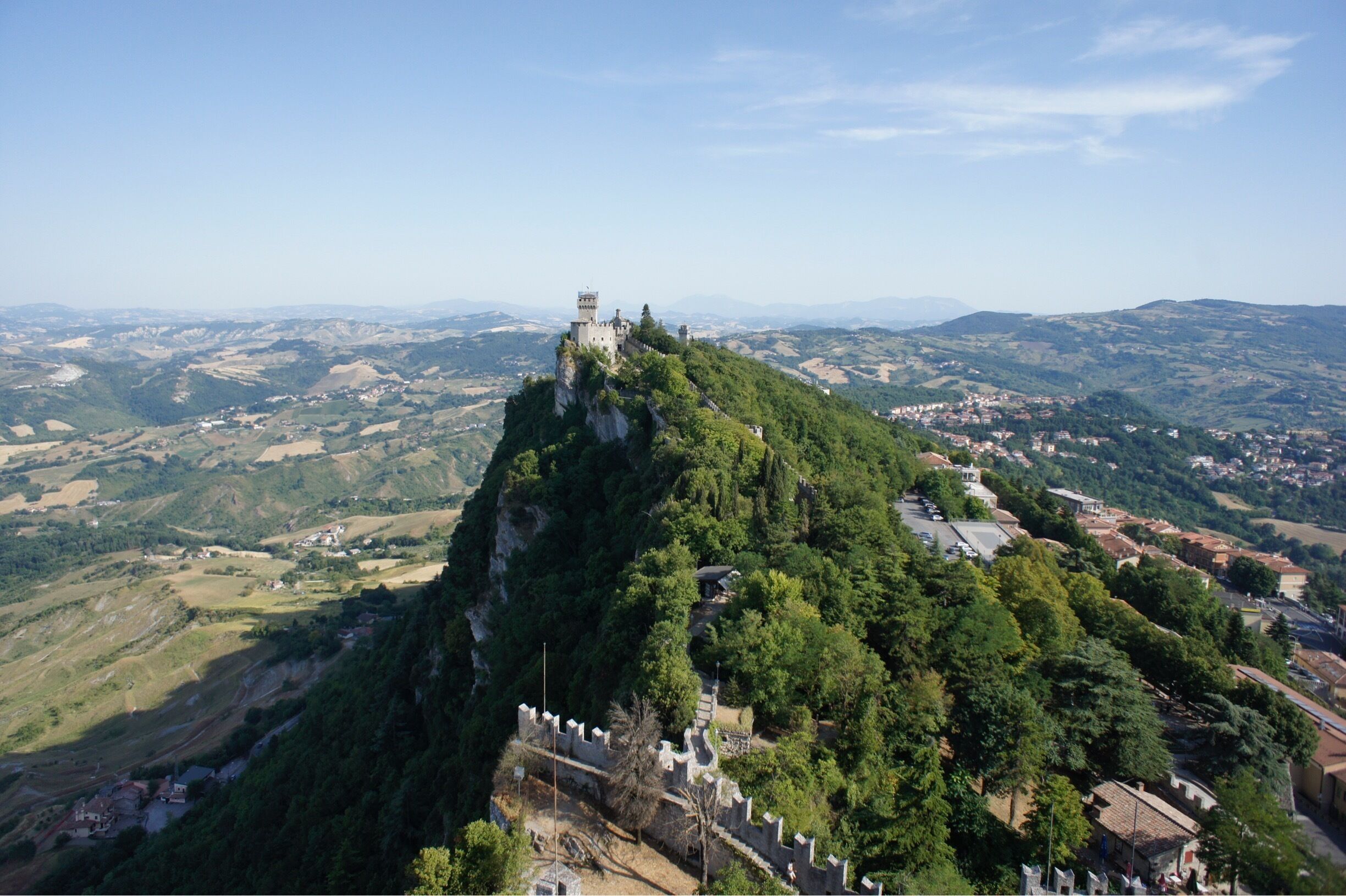 A castle on a hilltop overlooking a valley with scattered houses and fields.