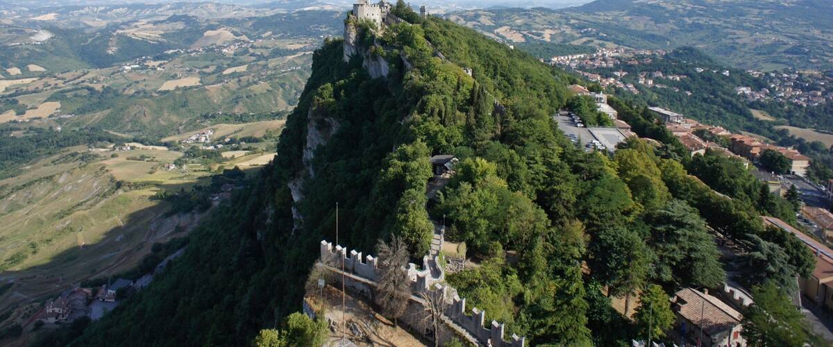A castle on a hilltop overlooking a valley with scattered houses and fields.