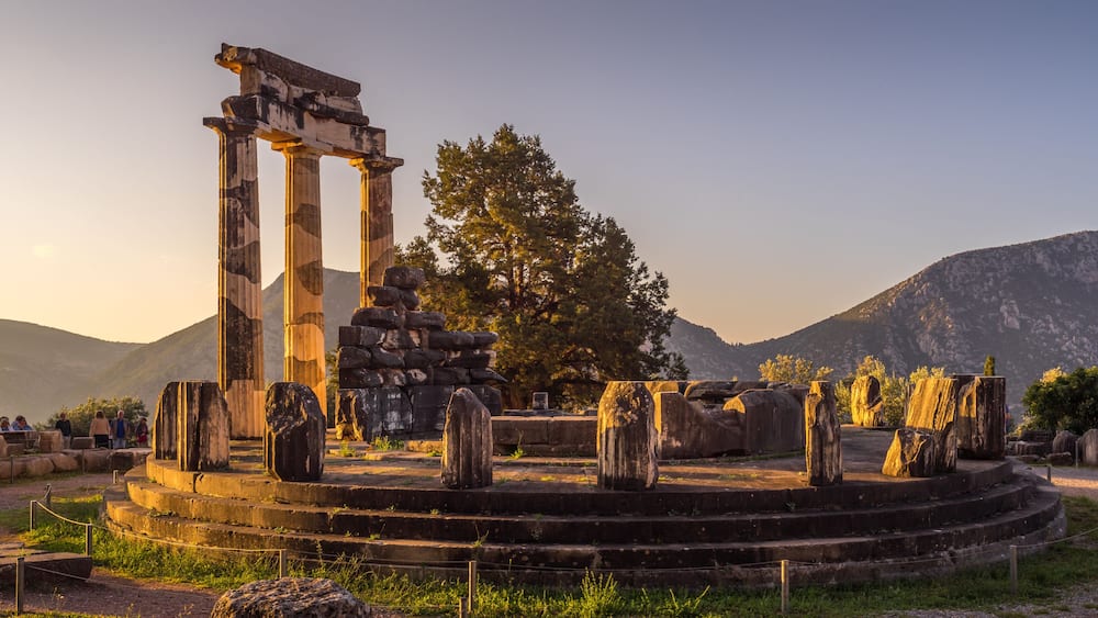 Ancient ruins with columns and stone structures, surrounded by a mountainous landscape.
