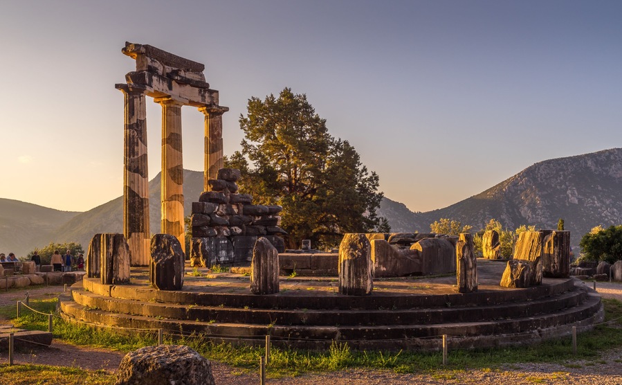 Ruinas antiguas con columnas y estructuras de piedra, rodeadas por un paisaje montañoso.