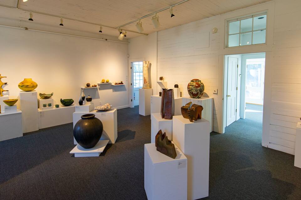 Une galerie d’art où sont exposées diverses sculptures et pièces de poterie sur des socles blancs.