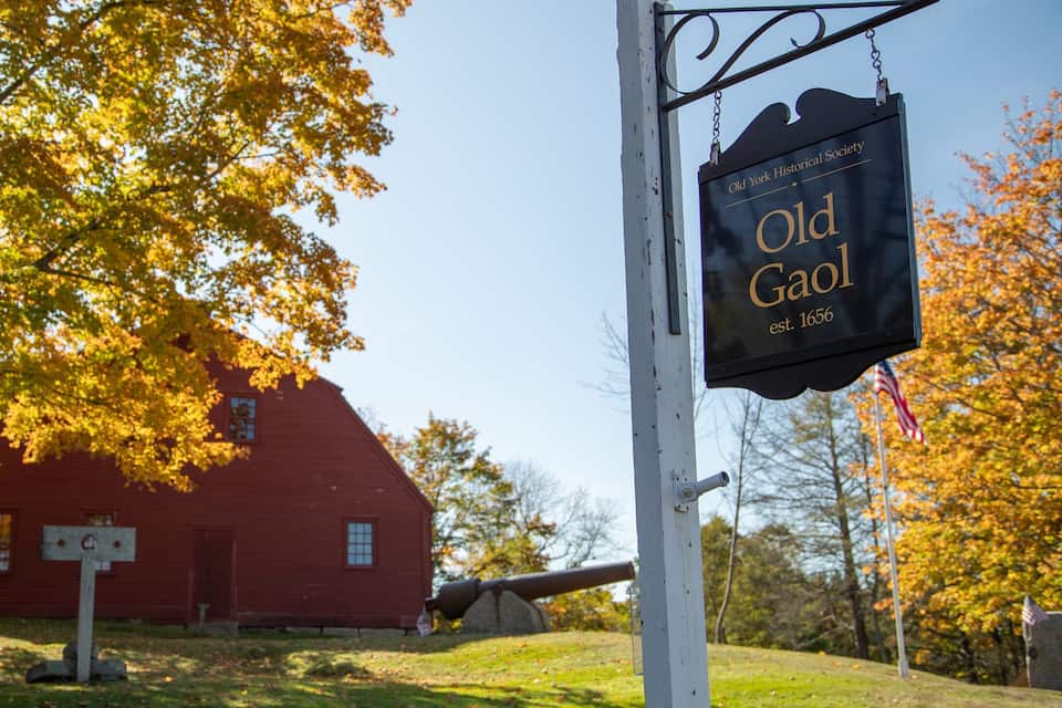 A red barn with a sign for Old Gool, established in 1656, and a cannon in the background.