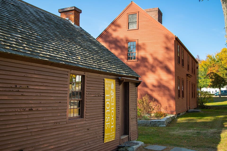 A wooden building with a sign reading "Stories in the Old House" and a red brick building in the background.