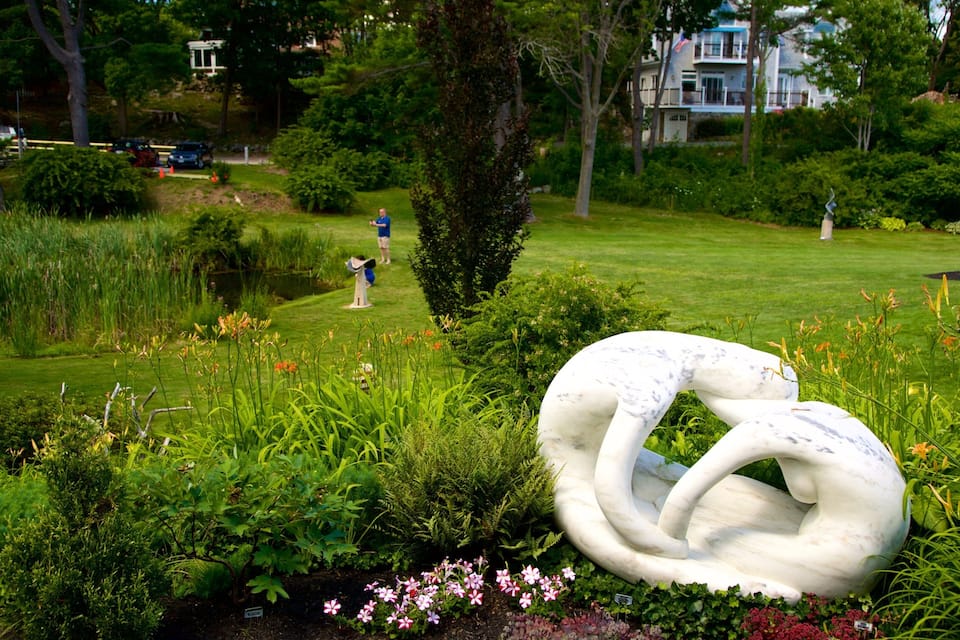 A garden with a large white sculpture, lush greenery, and a pond.