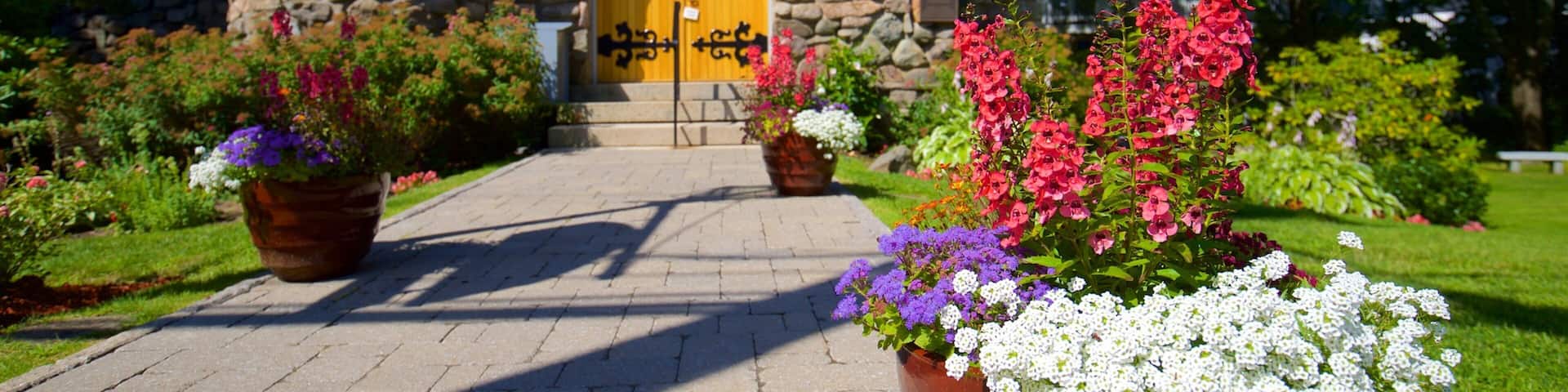 A stone building with a yellow door, surrounded by flower beds with pink, purple, and white flowers.