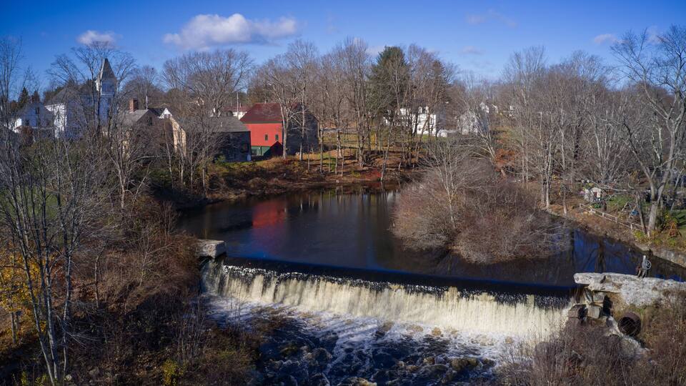 A dam with a waterfall, surrounded by trees and houses.