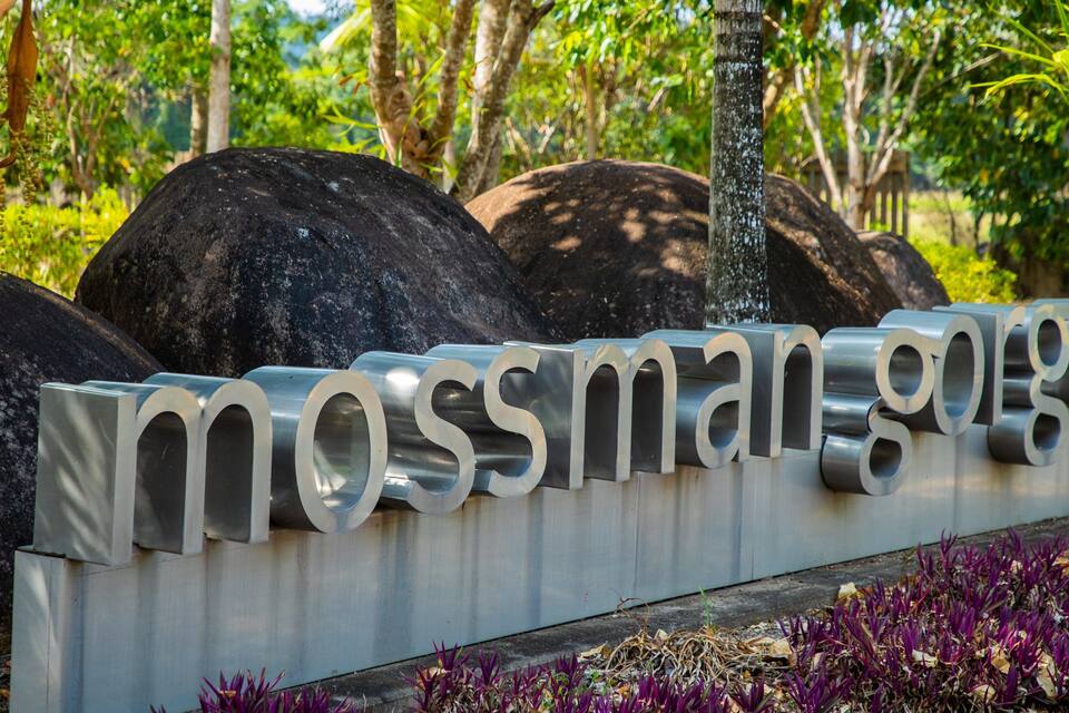Un senyal metàl·lic amb el text 'mossman gorge' envoltat de roques i vegetació.